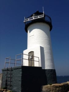 A white lighthouse with black trim and a blue sky in the background.