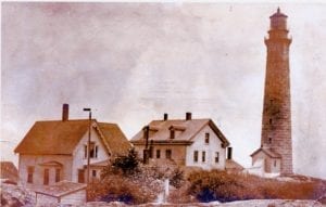 A picture of houses and water fountain in front of the lighthouse.