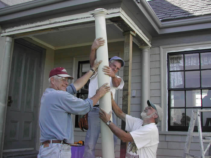 Three men working on a pole in front of a house.