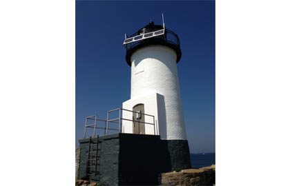 A white lighthouse with black trim and a ladder.
