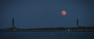 A full moon setting over the ocean with boats in it.