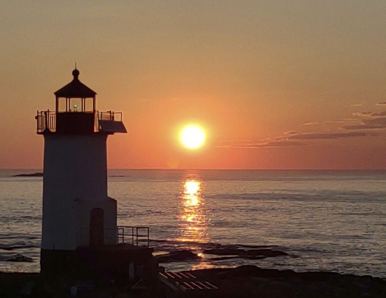 A lighthouse with the sun setting in the background.